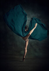 Portrait of beautiful ballerina dancing with fabric over dark background. Back view