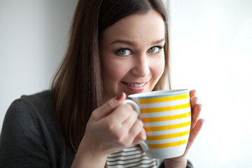 Beautiful young woman drinking tea by the window