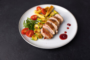 Grilled duck breast fillet with Brussels sprouts, mini corn, cherry tomatoes, arugula and lingonberry sauce. Traditional Mediterranean cuisine. Selective focus, close-up.