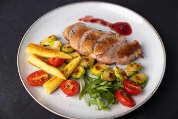 Grilled duck breast fillet with Brussels sprouts, mini corn, cherry tomatoes, arugula and lingonberry sauce. Traditional Mediterranean cuisine. Selective focus, close-up.