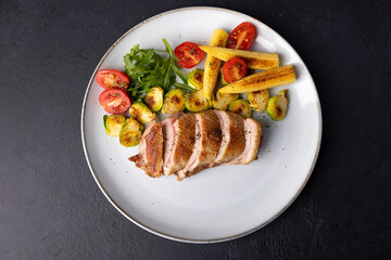Grilled duck breast fillet with Brussels sprouts, mini corn, cherry tomatoes and arugula. Traditional Mediterranean cuisine. Selective focus, close-up.