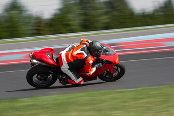 A motorcycle rider in leather suit riding on a red sport motorcycle through a corner at high speed....