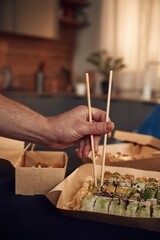 Obraz premium Using chopsticks. Man in casual clothes is with sushi that is in the paper eco box
