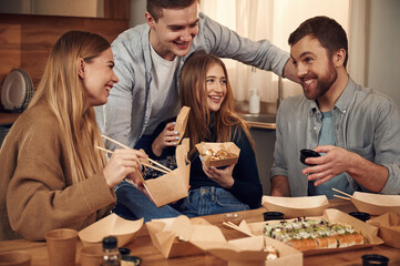 Having fun, casual conversation. Friends are sitting indoors at home and eating sushi together