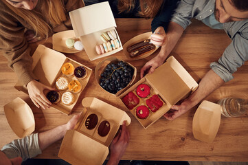 Top view of table with food on it, hands of the people taking it, eating. Macarons, blueberries, desserts, pastry meal