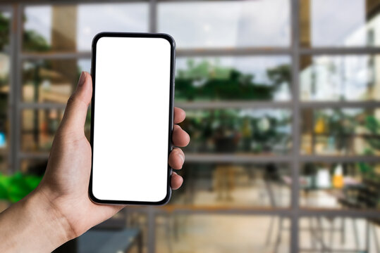 Mockup image of hand holding white mobile phone with blank white screen in cafe.