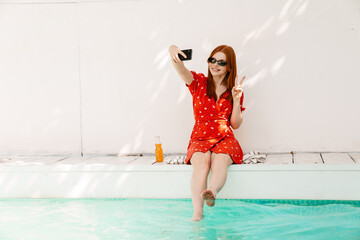 Beautiful woman taking selfie while resting by the swimming pool