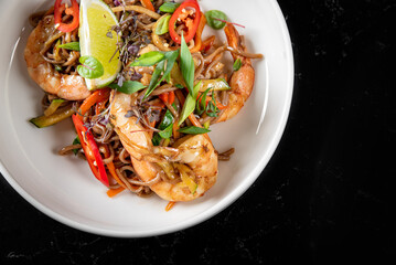 Stir fry noodles with vegetables and shrimps in plate on table background