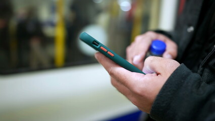 Close up person holding cellphone with train arriving at platform in background. Hands holding smartphone in foreground