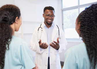 Smiling senior doctor talks to junior healthcare assistant, standing in hospital