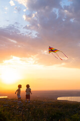 Fototapeta na wymiar two happy little kids boys having fun with kite in nature at sunset