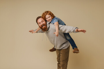 Cheerful father carrying his son on his back isolated over beige wall