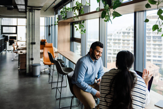 Indian business people talking while sitting near window in office