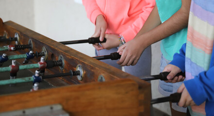 Children playing metegol. Foosball. Soccer hall game. Traditional game. Soccer game. Table with soccer players. Old wooden foosball. Football players. Dolls with blue and red painted T-shirts.