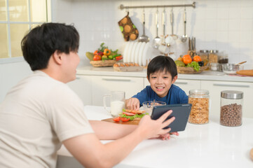 Young Asian father and his son using digital tablet enjoying together in kitchen at home