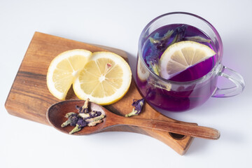 Chinese blue violet anchan tea in a glass cup and wooden spoon on a white background. Wooden board and lemon slices. Top view