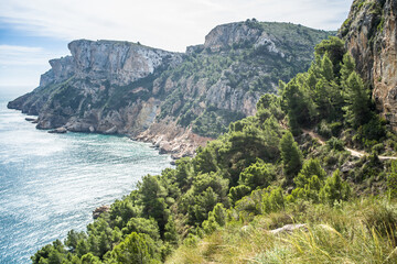 Fototapeta na wymiar Moraig pebble beach. cliffs, rocks, mountain path and view of the mediterranean sea on a beautiful sunny day 