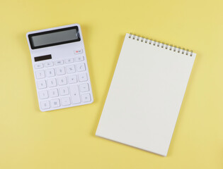  flat lay of white calculator with blank page opened notebook on yellow background. business and education concept.