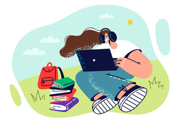 Student girl with laptop sits on green lawn in sunny weather and watches online webinar