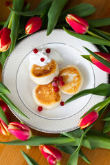 Homemade cottage cheese cheesecakes with sour cream and red currant berries with red tulips