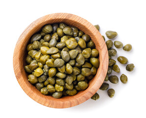 Capers in a wooden plate and scattered on a white background. Top view