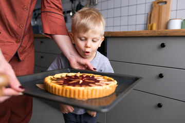 cooking fruit and berry pie at home, child blowing on hot pan