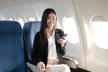Fototapeta na wymiar Traveling and technology. Flying at first class. Pretty young Asian business woman using smartphone while sitting in airplane.