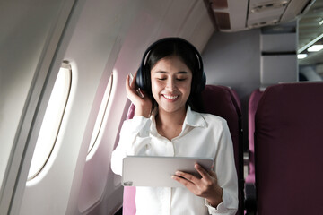 Joyful asian woman sits in the airplane using laptop and listen music while go to travel