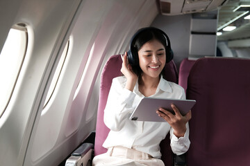 Joyful asian woman sits in the airplane using laptop and listen music while go to travel