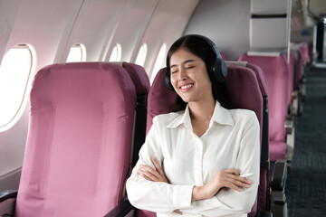 Young female listening favourite songs during flight in first class cabin using mobile playlist and accessory, woman entertaining on airplane board enjoying music in headphones from smartphone