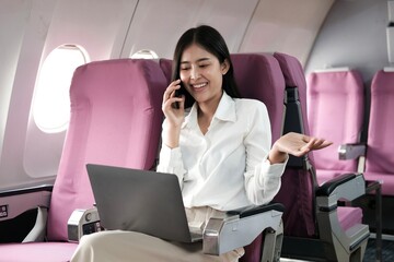 Asian woman passenger sitting in airplane near window and reading news from social networks or using travel applications in smartphone