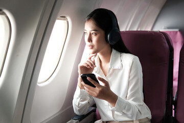 Joyful asian woman sits in the airplane and using tablet while go to travel