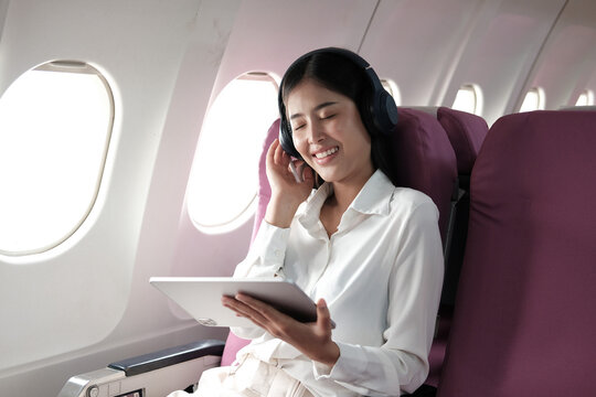 Joyful asian woman sits in the airplane and listen music while go to travel