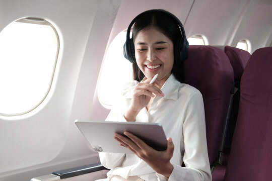 Joyful asian woman sits in the airplane using laptop and listen music while go to travel