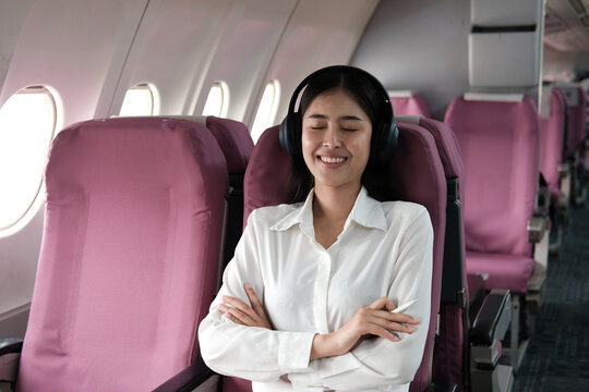 Young female listening favourite songs during flight in first class cabin using mobile playlist and accessory, woman entertaining on airplane board enjoying music in headphones from smartphone