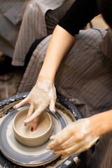 Hands of woman stained with pottery clay. She is making pottery or ceramic on potter's wheel  