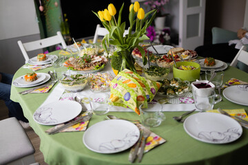 Home interior with easter decor. Spring flowers in a vases. Traditional Easter dishes with white borscht, sausage, eggs, salad and cakes on festive table in Poland
