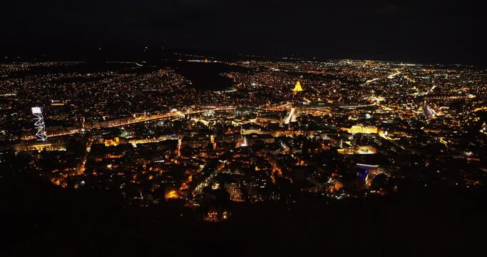 Tbilisi. Panorama of night city in light of night lights. Tbilisi Holy Trinity Cathedral in center of city stands out with bright yellow lighting against the backdrop of bright city night lighting