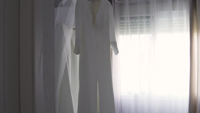 Slow motion tilting shot revealing a stunning long white bridal dress hanging