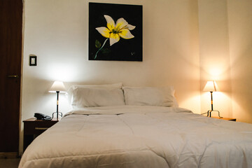 White hotel bed with a yellow flower painting on the wall