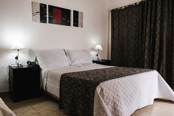 Hotel bedroom with black and white bed, lamps, curtains and painting on the wall