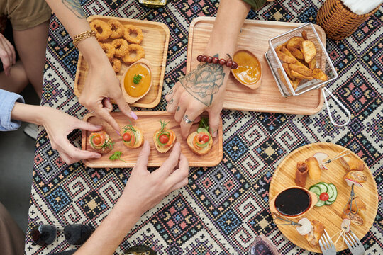 Hands of people taking snacks from wooden plates view from above