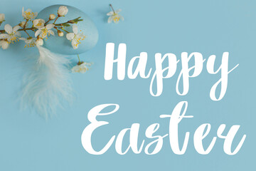 Happy Easter text sign on easter egg and spring blossom on blue background flat lay. Modern Easter greeting card. Handwritten lettering