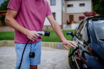 Man holding power supply cable at electric vehicle charging station.