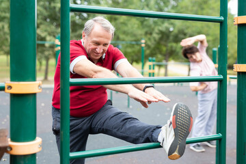 Obraz premium Elderly man doing leg stretching on the outdoor sports ground
