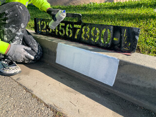 City worker painting address on street curbs using stencil numbers with white and blank paint
