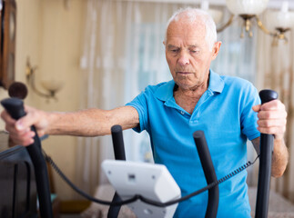 Fit senior man at home doing cardio work out on an elliptical machine