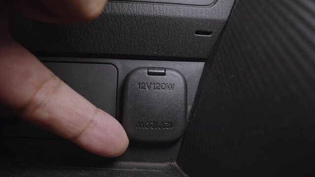 Closeup of finger open 12 volt 120 watt charger socket for electronic equipment in car.