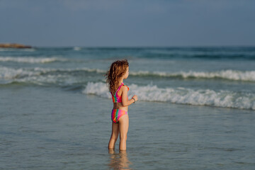 Fototapeta na wymiar Little girl in swimsuit standing in sea, enjoying holiday.