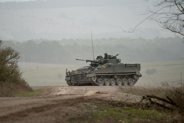 British army Warrior FV510 with commander in action, moving across countryside